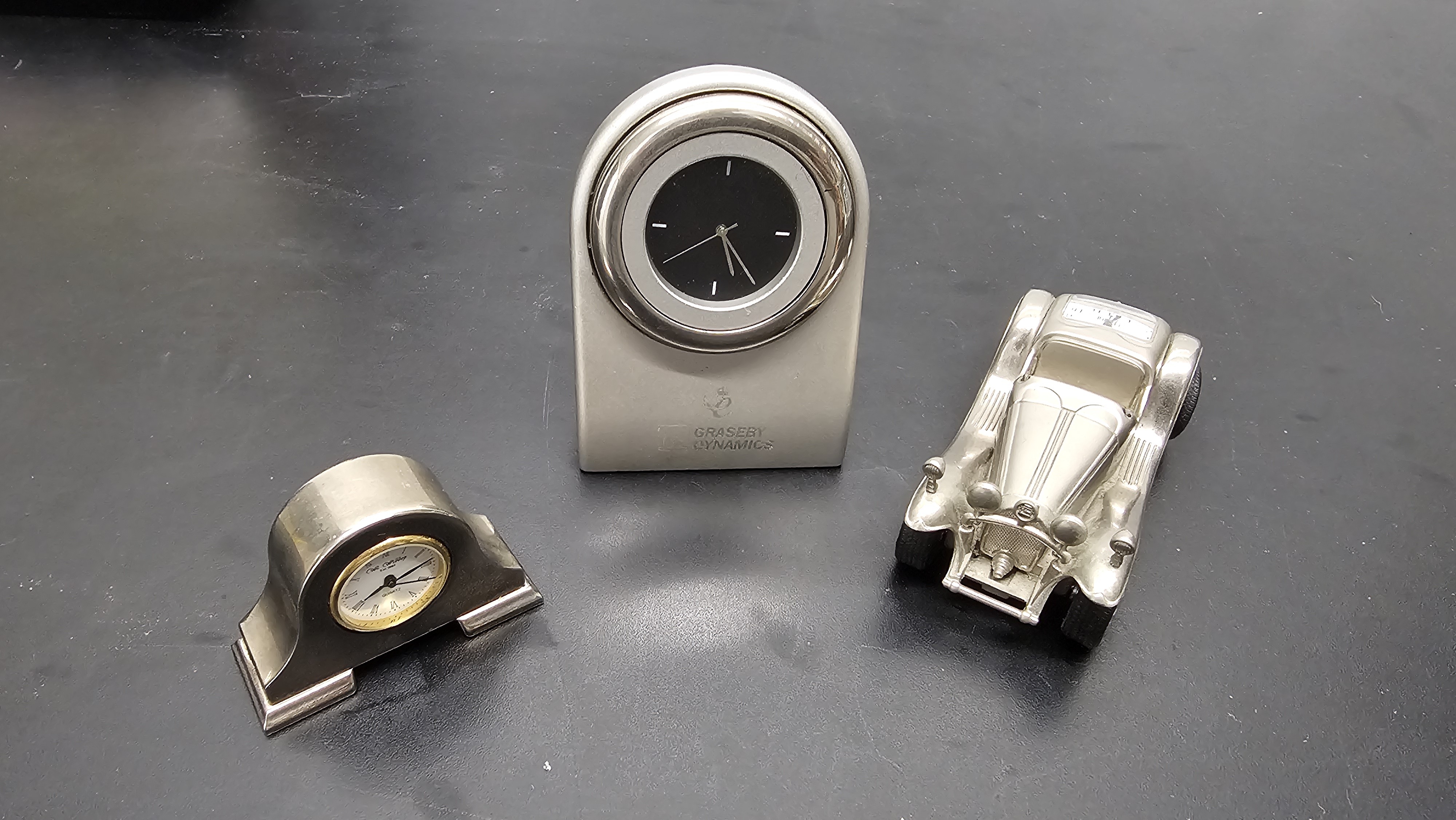 A Trio of Silver-Toned Novelty and Corporate Desk Clocks including Colibri and Graseby Dynamics