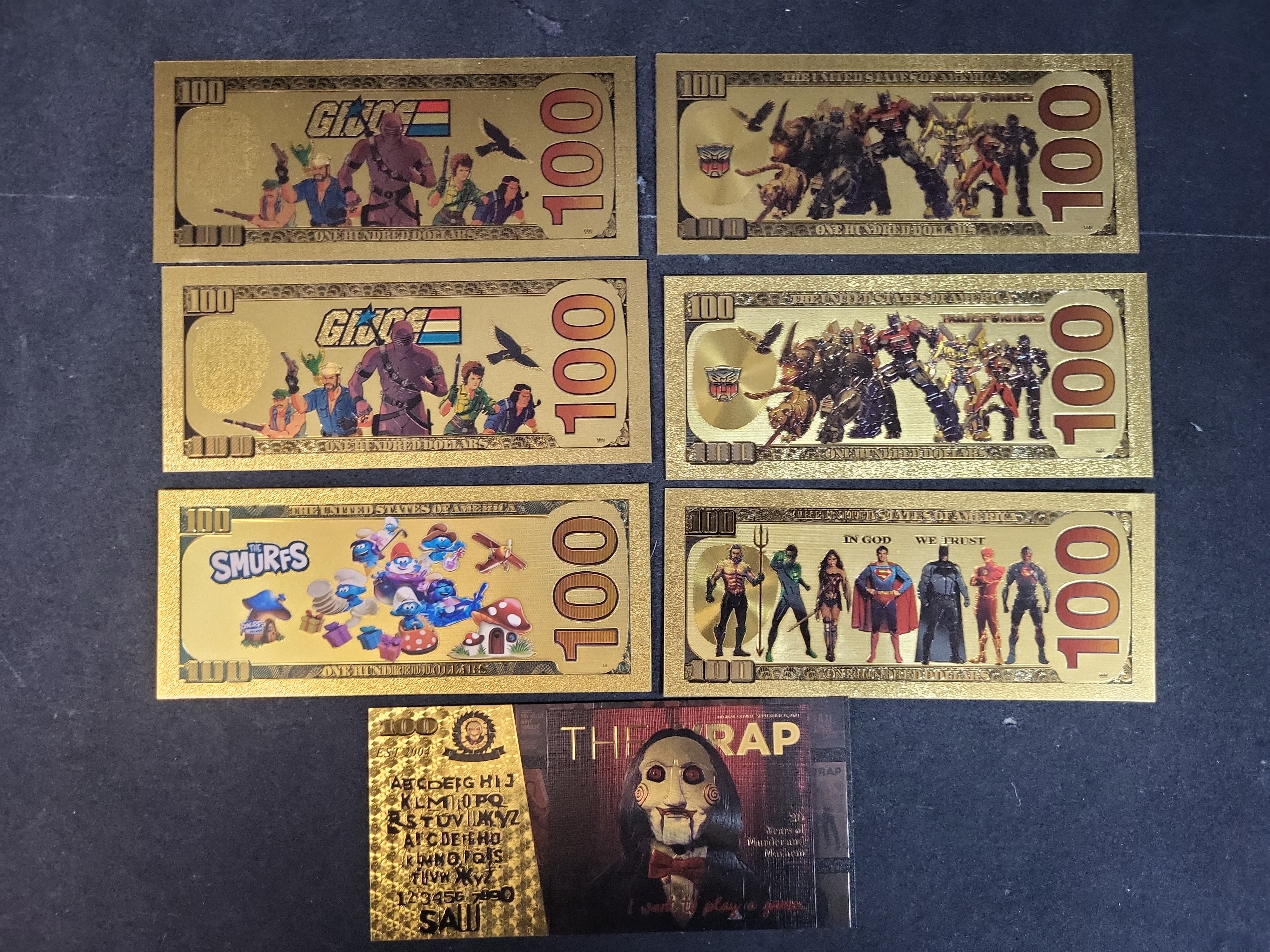 I03653 | Seven Novelty Gold Foil Banknotes Featuring G.I. Joe, Transformers, The Smurfs, and Cinematic Characters