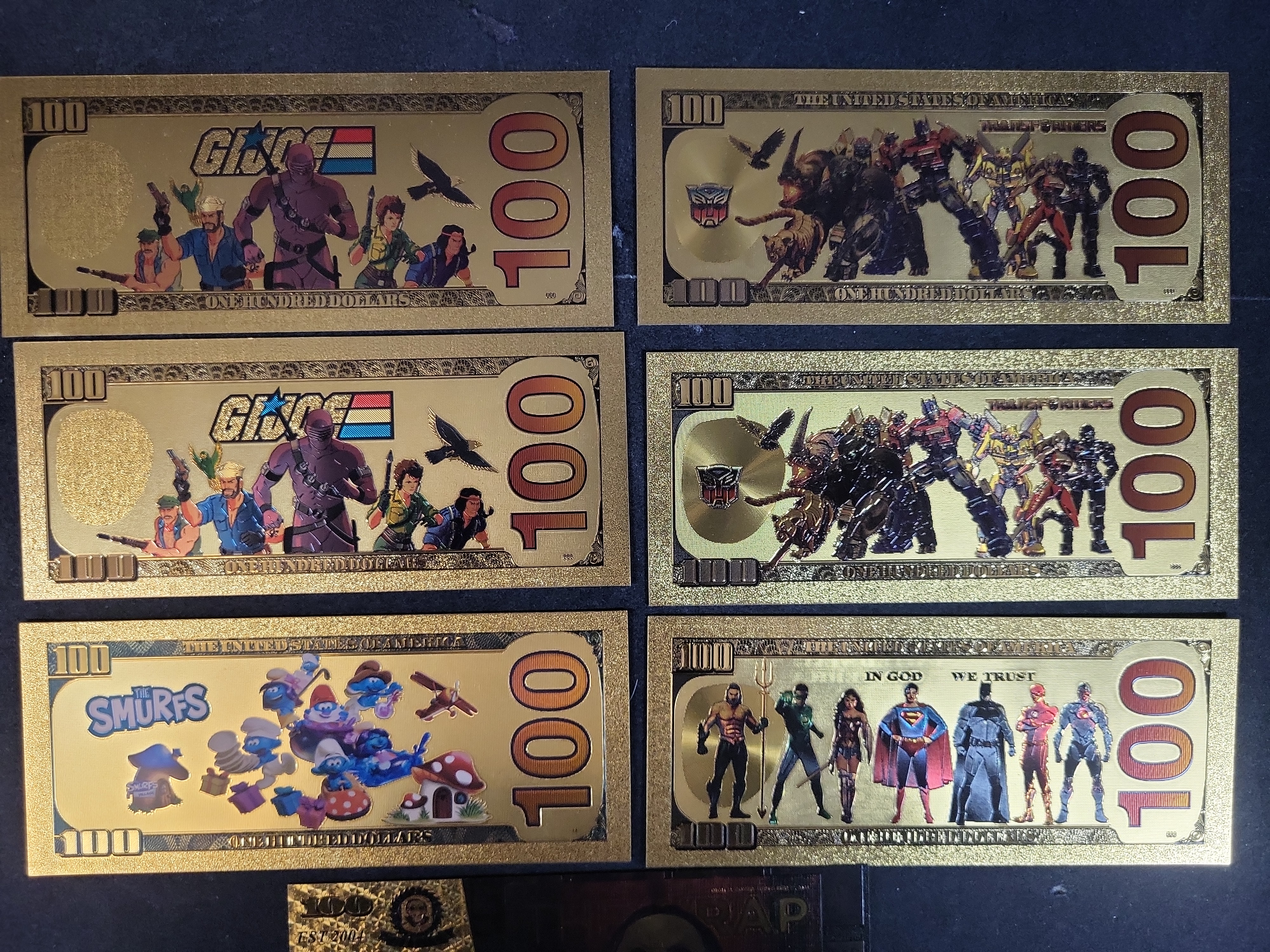 I03653 | Seven Novelty Gold Foil Banknotes Featuring G.I. Joe, Transformers, The Smurfs, and Cinematic Characters