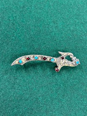A white metal brooch in the shape of a sabre with inset stones