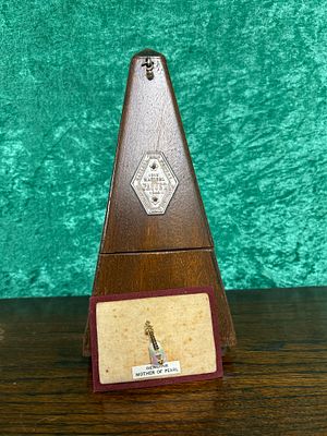A Maelzel Paquet Metronome together with a small, mother of pearl brooch in the shape of a guitar
