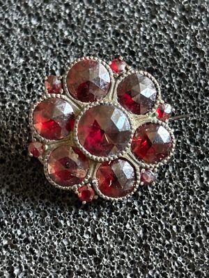 A small brooch or lace pin of circular design with garnets of varying sizes