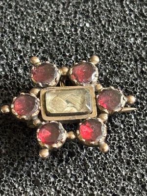 An antique mourning brooch / pendant with six garnets surrounding an inset panel containing a 