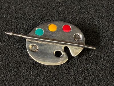 A silver brooch in the shape of an artists paint palette (some colours missing)