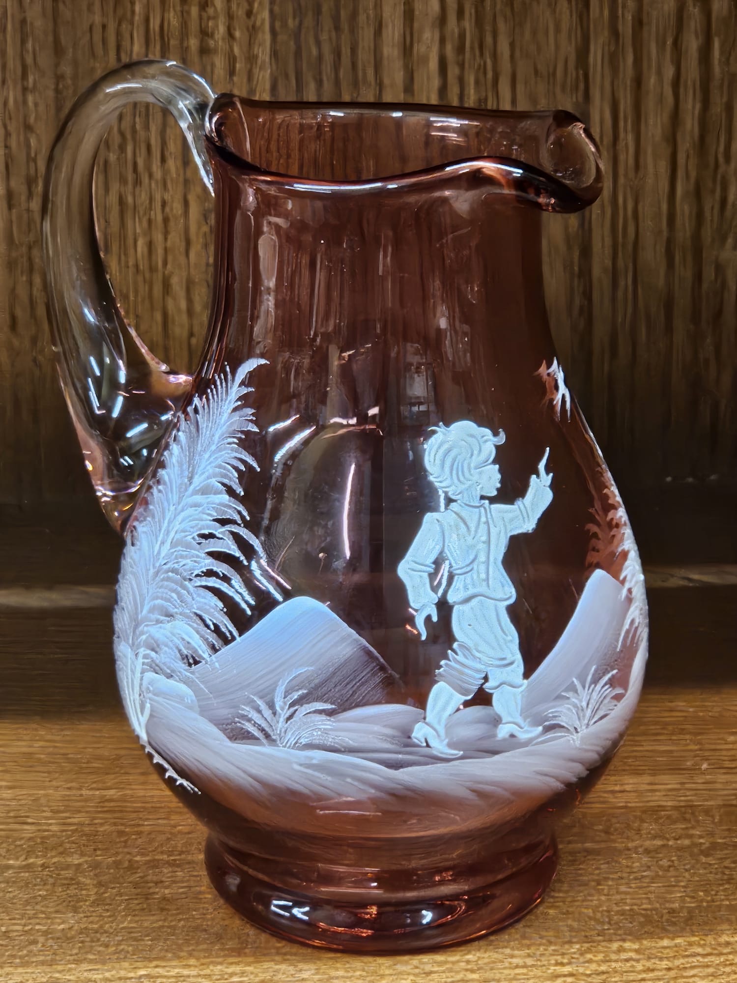 An amethyst glass pitcher with white enamel decoration of a boy in a landscape