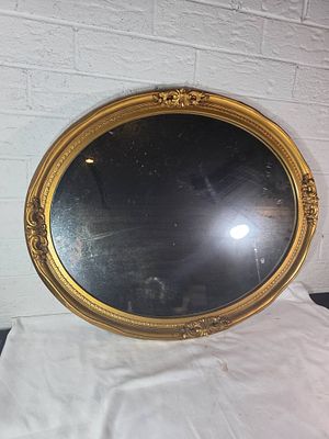 Gold-Plated Oval Wall Mirror. An oval wall mirror with a gold-plated frame featuring ornate