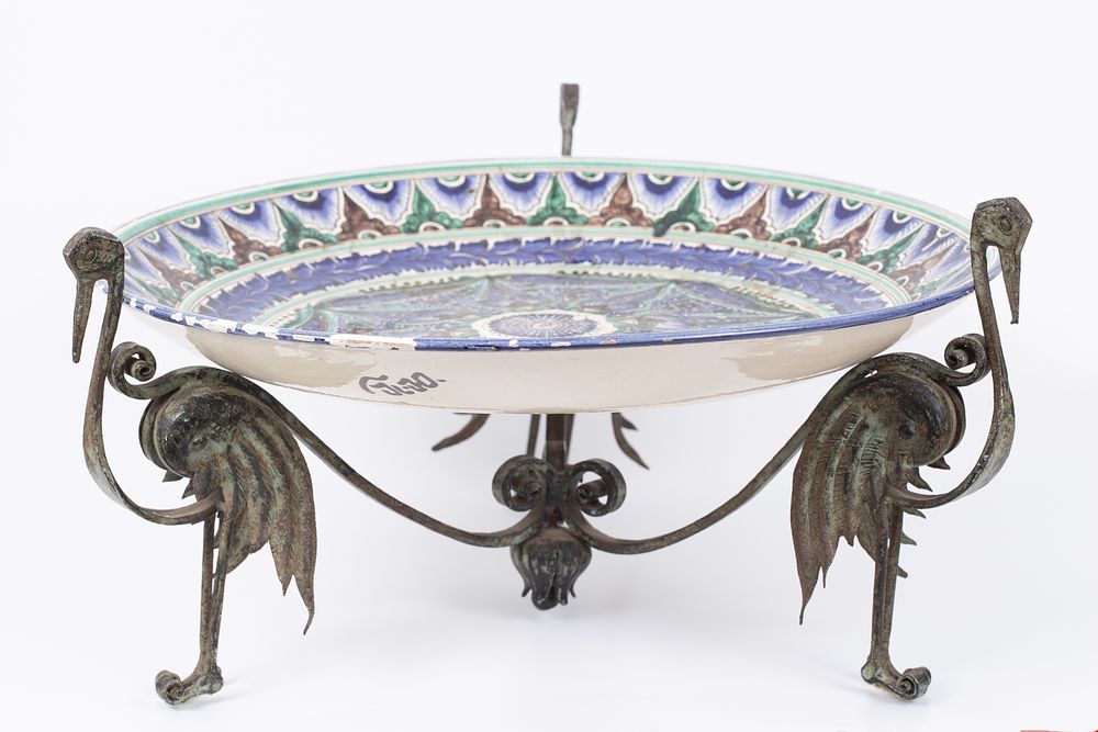 A large painted bowl placed on a metal stand with a bird pattern. A European ceramic bowl 