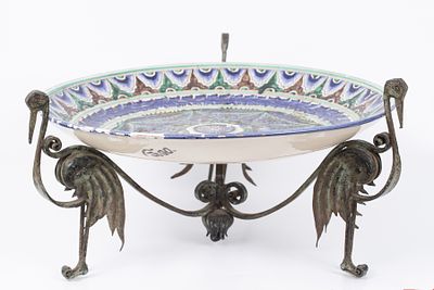 A large painted bowl placed on a metal stand with a bird pattern. A European ceramic bowl 