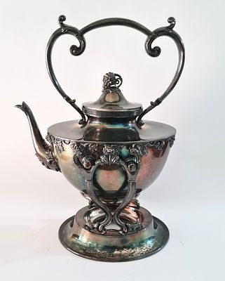 קומקום מצופה כסף על גבי מעמד מתנדנד ( מאפשר הצבת פתלית חימום ) סגיון הברוק . תוצרת ארה"ב 