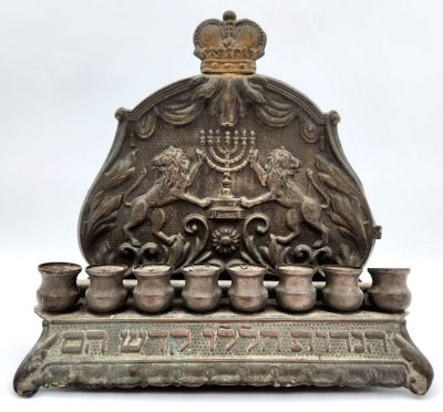 חנוכיית גב ישנה מאוד מנחושת, מעוטרת ריקוע של אריות, מנורה וכיתוב, ללא שמש. 
מידות: 19X20 ס"מ.