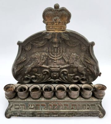 חנוכיית גב ישנה מאוד מנחושת, מעוטרת ריקוע של אריות, מנורה וכיתוב, ללא שמש. 
מידות: 19X20 