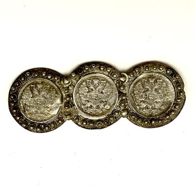 Брошь — 3 двадцатикопеечные монеты, 1910 год. 
Оправлены серебряной рамкой со сканью. 
Размер 