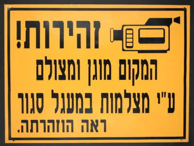 שלט עשוי פח - "זהירות! המקום מוגן ומצולם.... ראה הוזהרתה." (ראה הוזהרת כתוב עם עוד תוספת ה' 