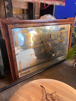 A Cadbury's advertising mirror in a decorated and carved frame. 95cm wide.