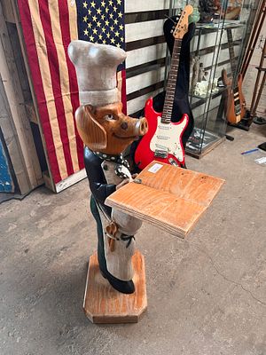 A dumb waiter of a pig in costume holding cook book. 3ft high