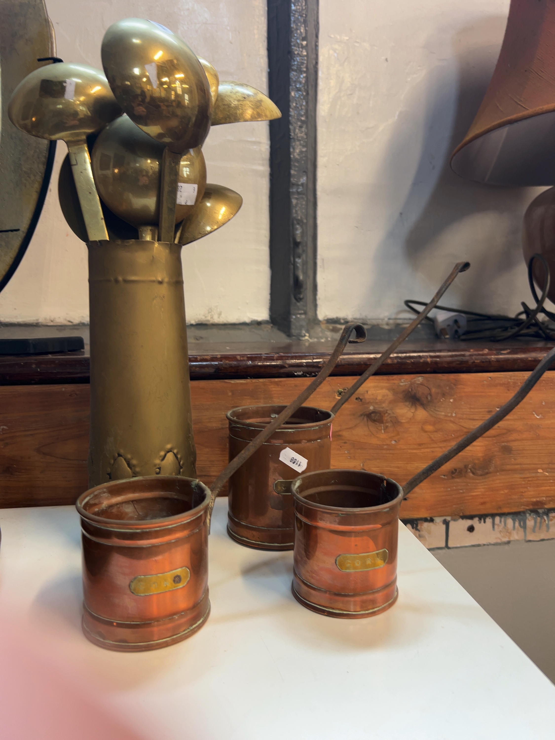 A Trio of Graduated Copper Corn Measures and a Collection of Brass Ladles in a Brass Vessel