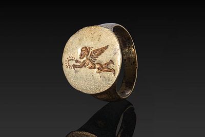 GREEK SOLID GOLD RING WITH FLYING EROS. Ca. 300 BC. A gold ring with a flat-section, tapering 