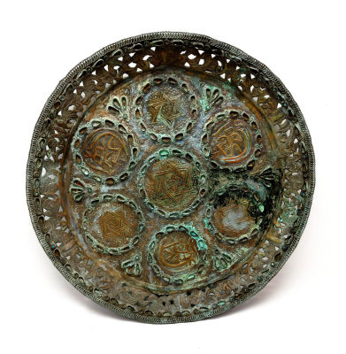 קערת ברונזה ישנה, מעוטרת מגני דוד ועיטורים נוספים. קוטר -33 ס''מ . קרע קיים בחלקה התחתון.