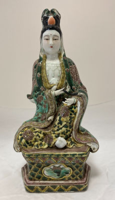 Китайская фарфоровая статуэтка богини Гуань Инь в сидячей позе; одна рука покоится на колене 
