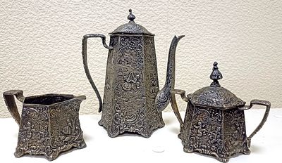 Чайный комплект из трех предметов: чайник, сливочник, сахарница. Предметы изобильно украшены 