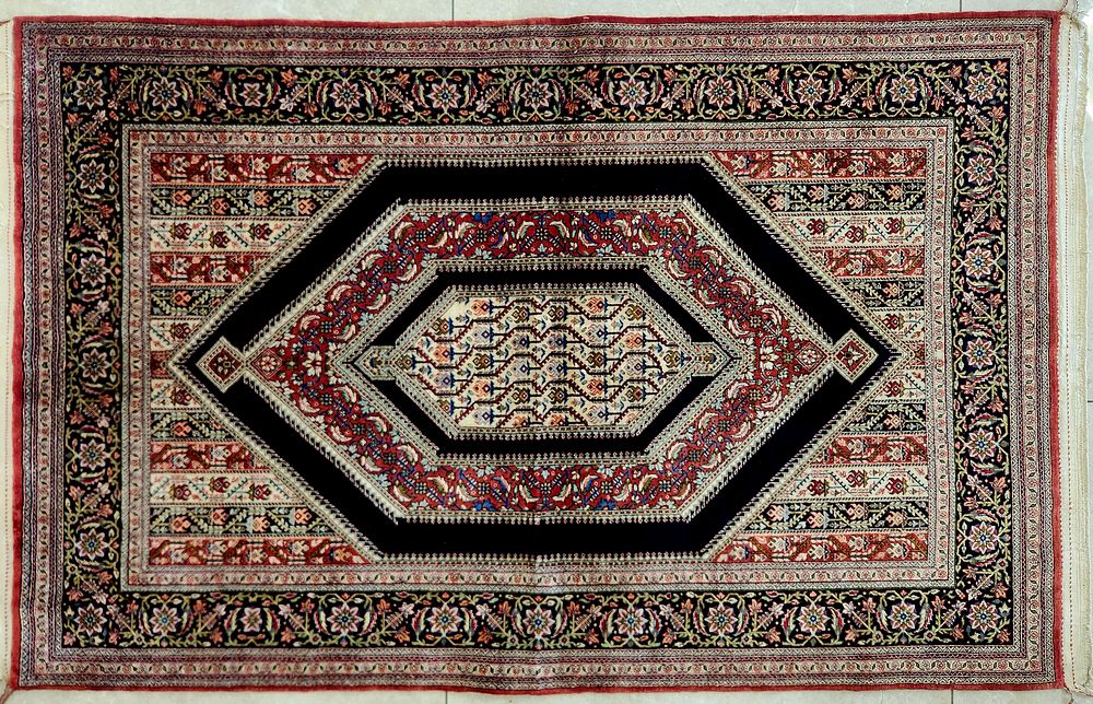 שטיח משי קום פרסי, 
איכותי במיוחד, 
דגם מעוינים ומוטיבים חוזרים על רקע צבעוניות מרשימה. 
צפיפות 