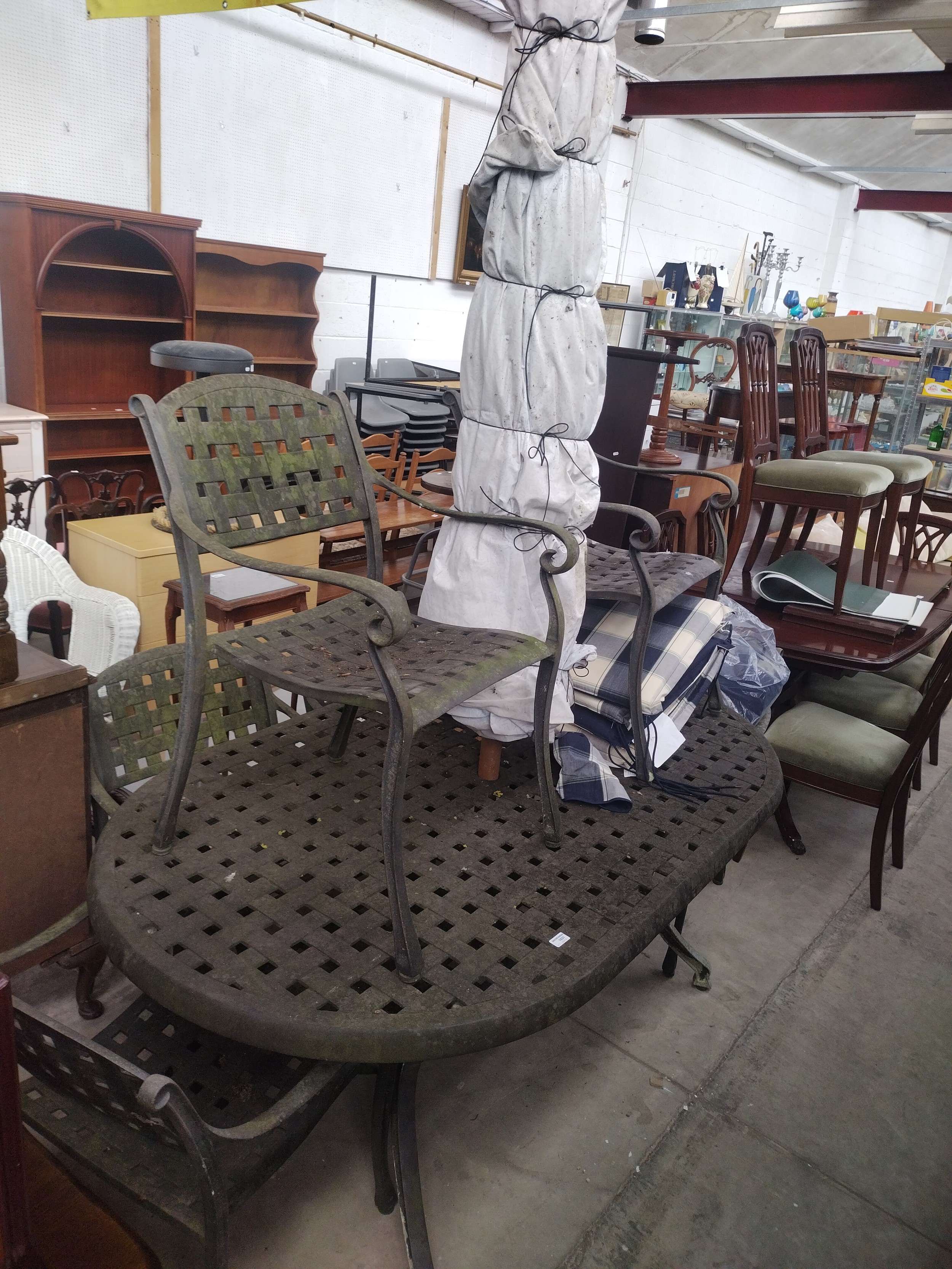 A large cast metal patio table with 6 x chairs, parasol and cushions