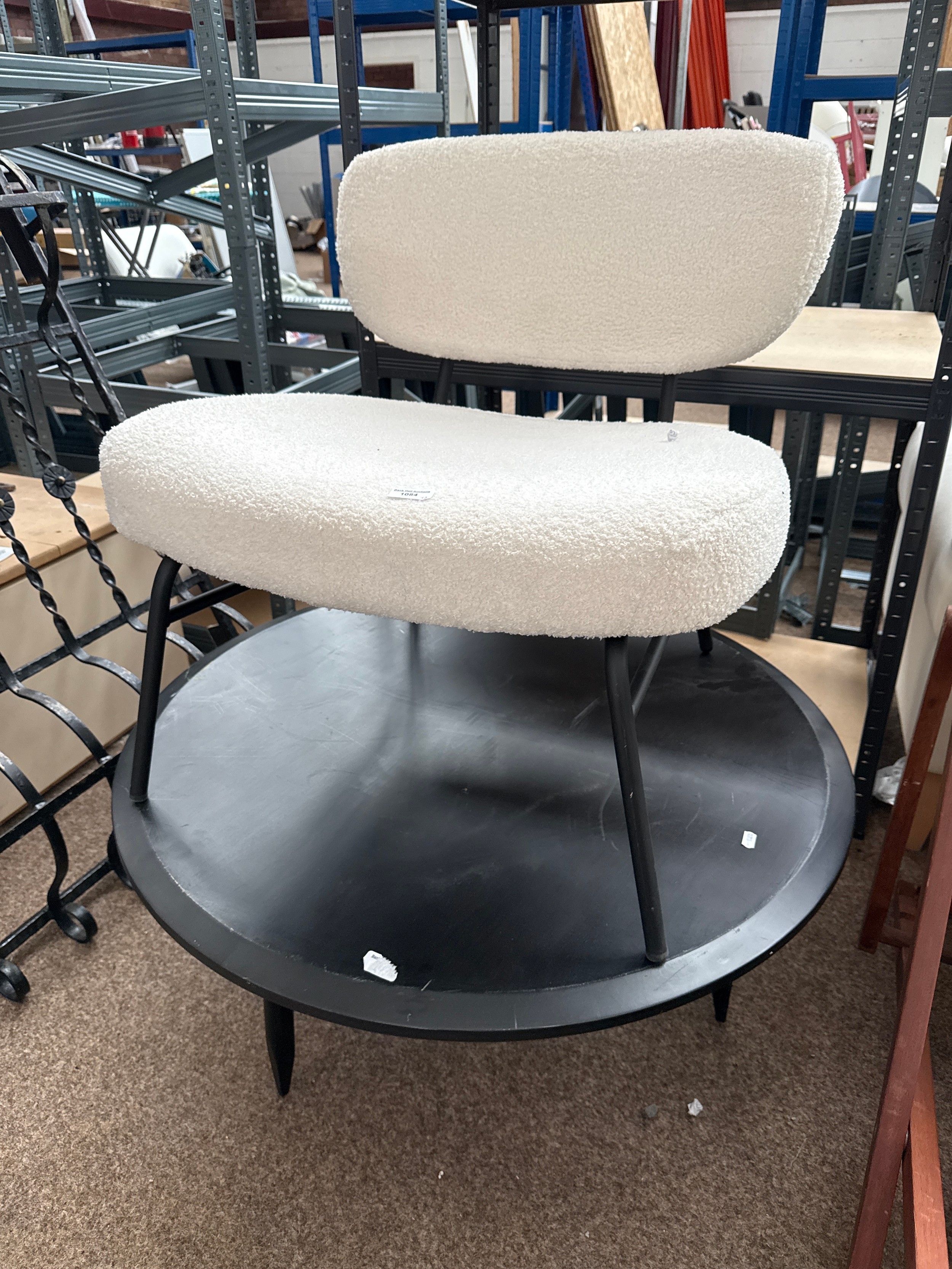 A large circular black coffee table and a large upholstered metal framed chair