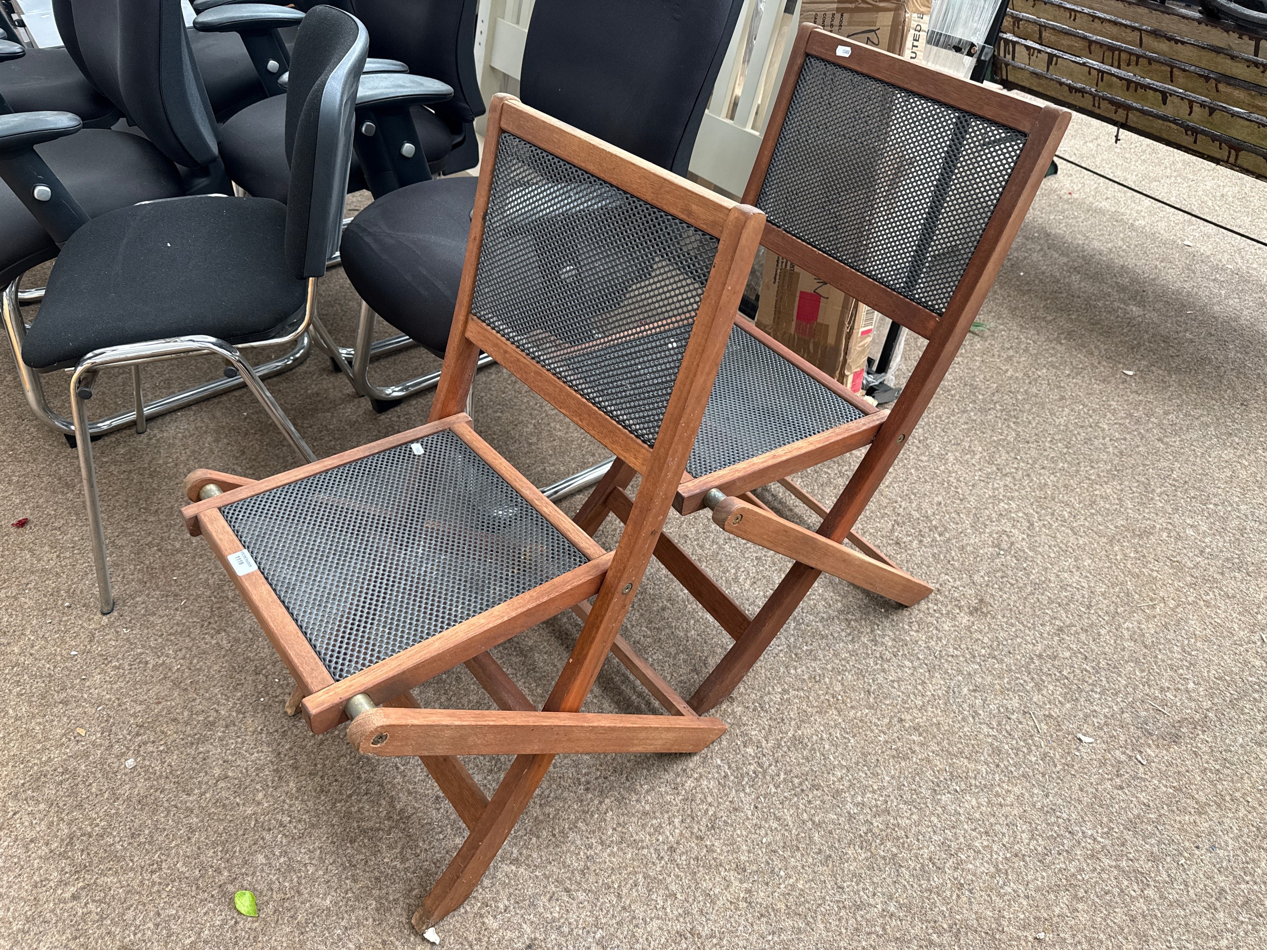 A pair of folding wooden chairs with metal grill panels