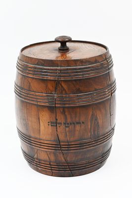 קופסה גדולה ומרשימה בצורת חבית, עם מכסה נשלף שבמרכזו ידית. על דופן הקופסה כיתוב המילה 