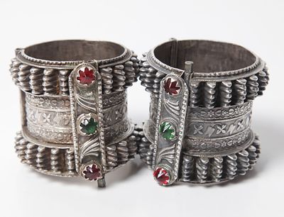 A pair of bracelets for a woman made of silver and red and green gems. Decorated with a ballet 
