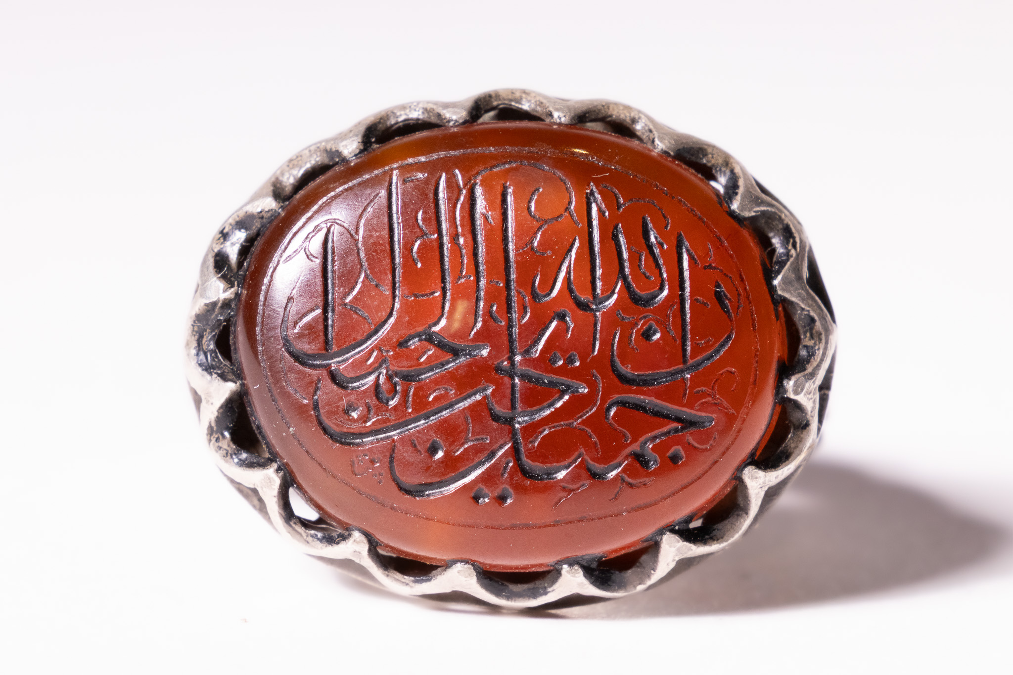 AN ISLAMIC WHITE METAL AND ENGRAVED CARNELIAN AGATE TALISMANIC SIGNET RING.