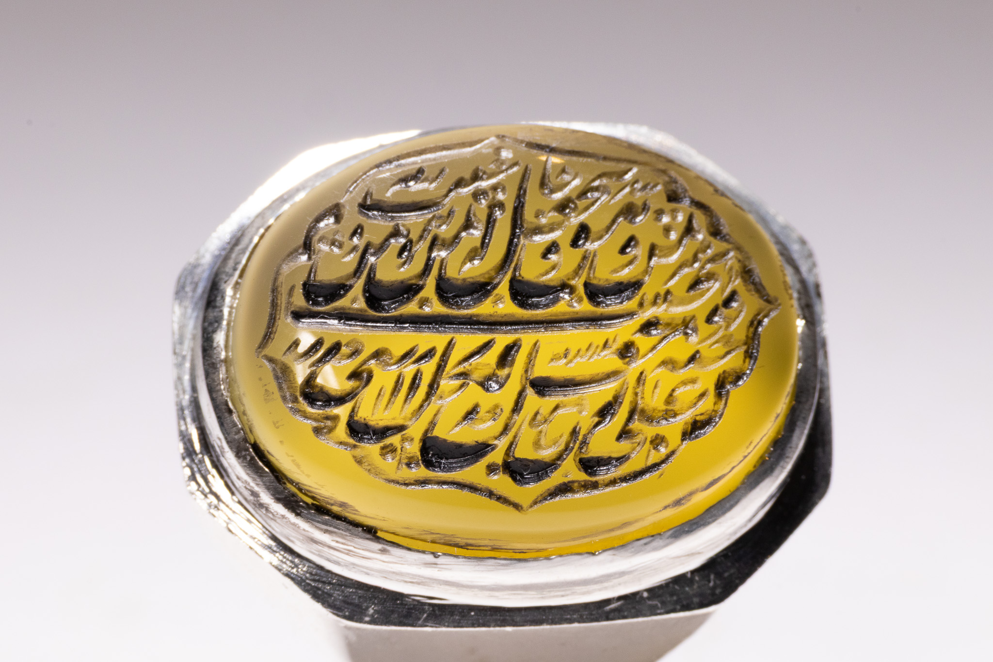 AN ISLAMIC WHITE METAL SIGNET RING WITH YELLOW AGATE INSCRIBED WITH SURAH AL-IKHLAS.