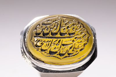 AN ISLAMIC WHITE METAL SIGNET RING WITH YELLOW AGATE INSCRIBED WITH SURAH AL-IKHLAS. A 