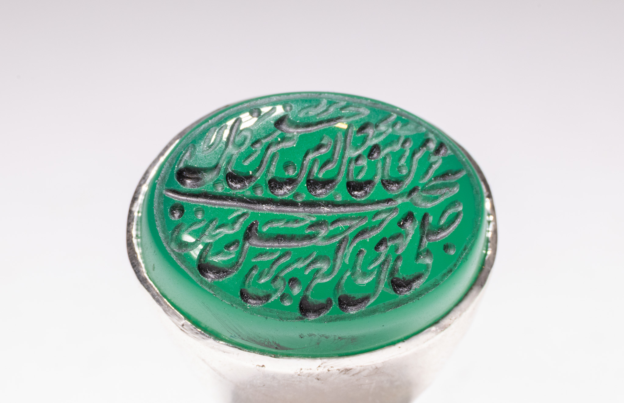 AN ISLAMIC WHITE METAL AND INSCRIBED GREEN AGATE SIGNET RING.