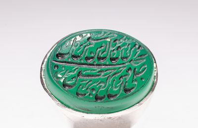 AN ISLAMIC WHITE METAL AND INSCRIBED GREEN AGATE SIGNET RING. An Islamic signet ring comprising 