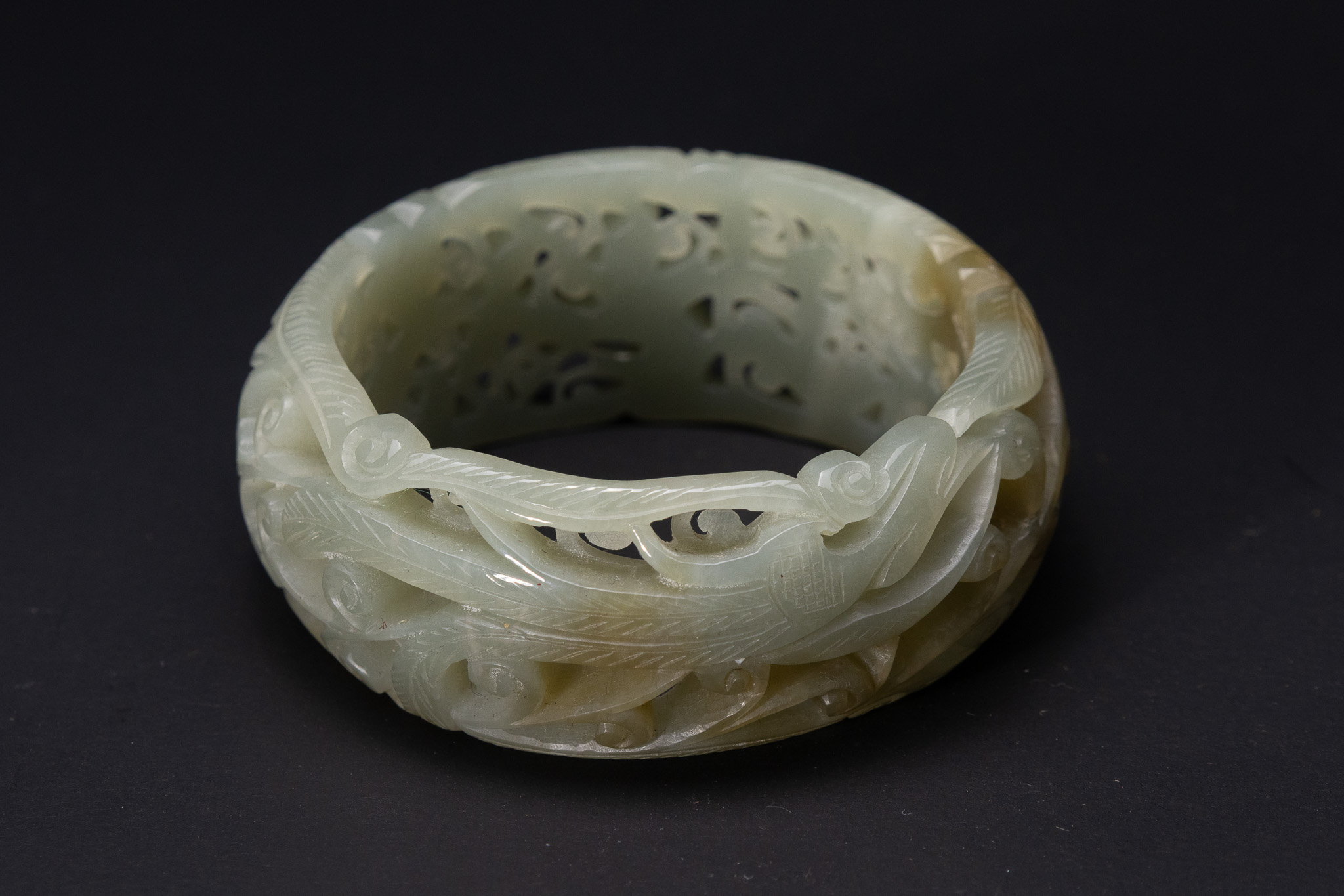A CHINESE RETICULATED PALE CELADON NEPHRITE JADE PHOENIX AND FLORAL BANGLE.