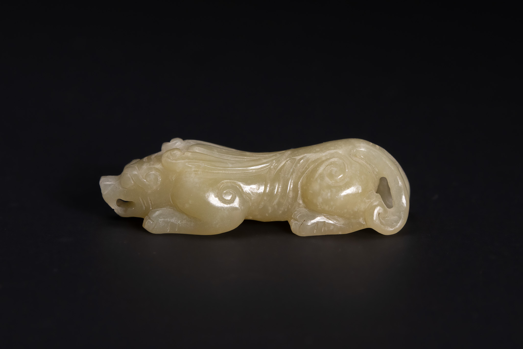 A CHINESE CARVED PALE CELADON JADE FIGURE OF A RECUMBENT BIXIE.