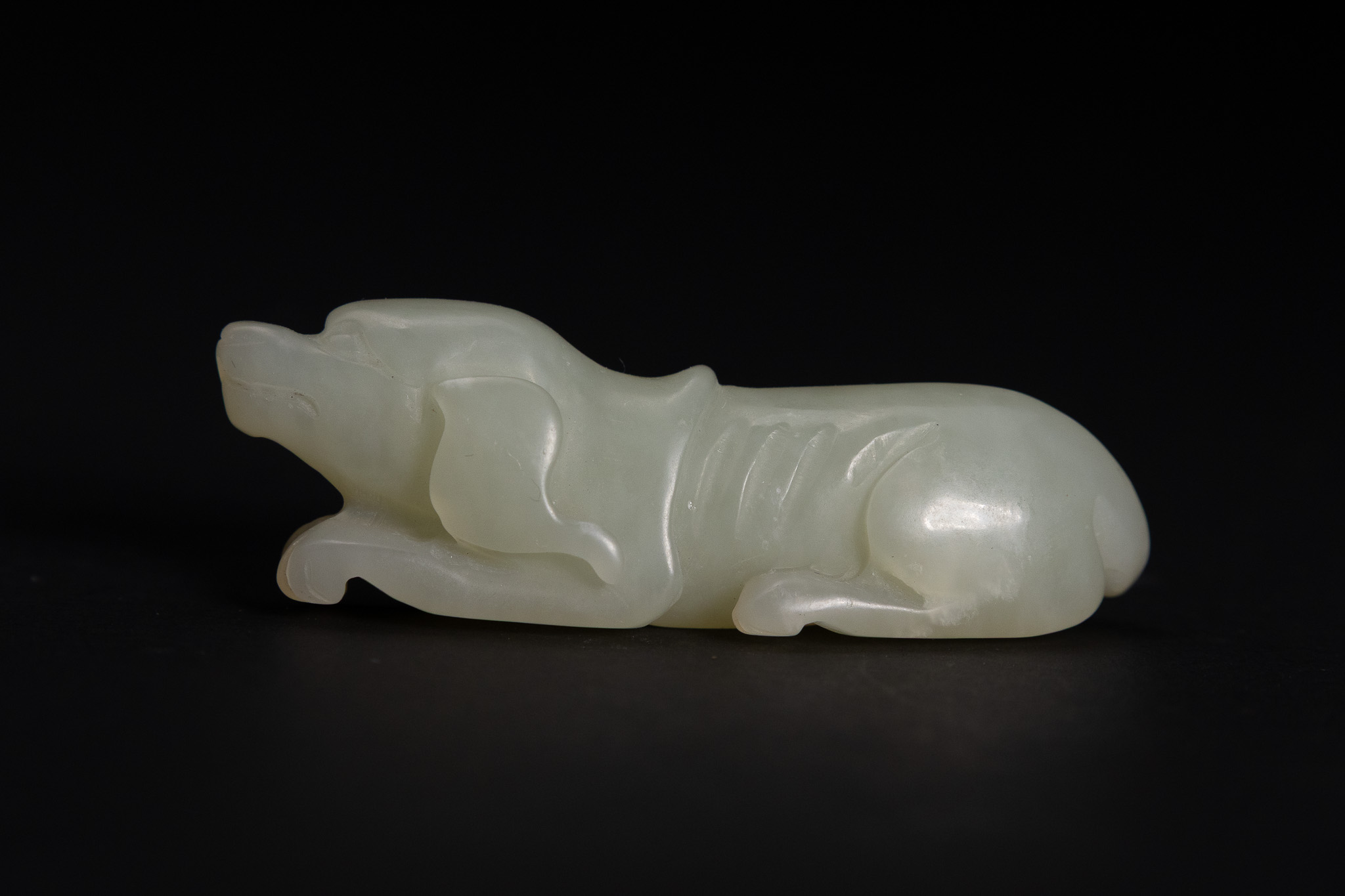 A CHINESE PALE CELADON JADE CARVING OF A RECUMBENT HOUND
