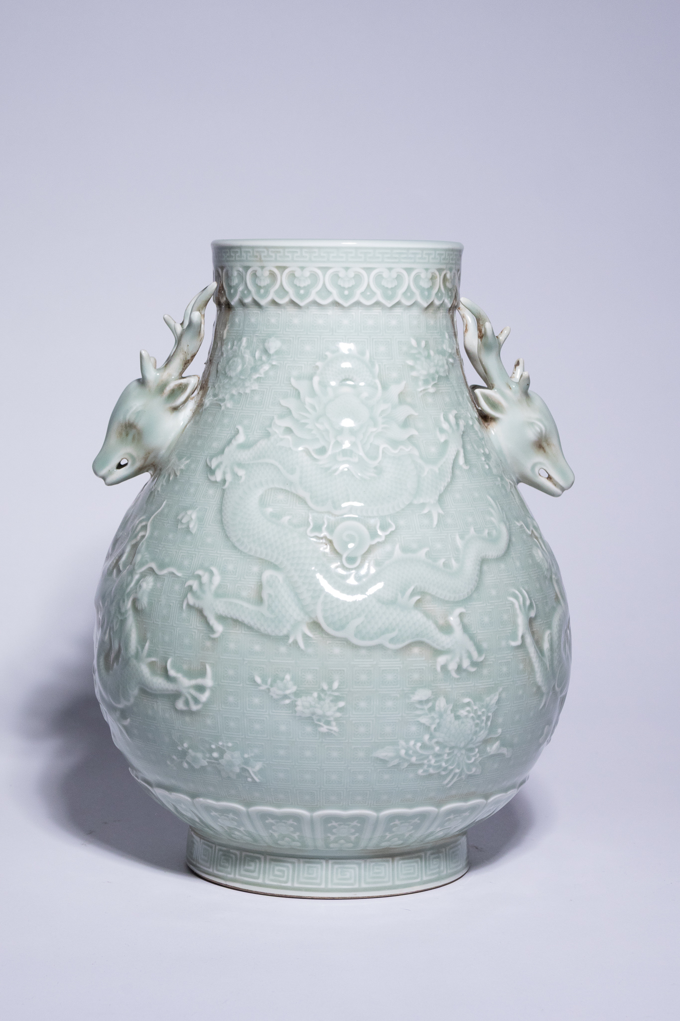 A CHINESE CELADON-GLAZED RELIEF-DECORATED DRAGON VASE WITH DEER-HEAD HANDLES.