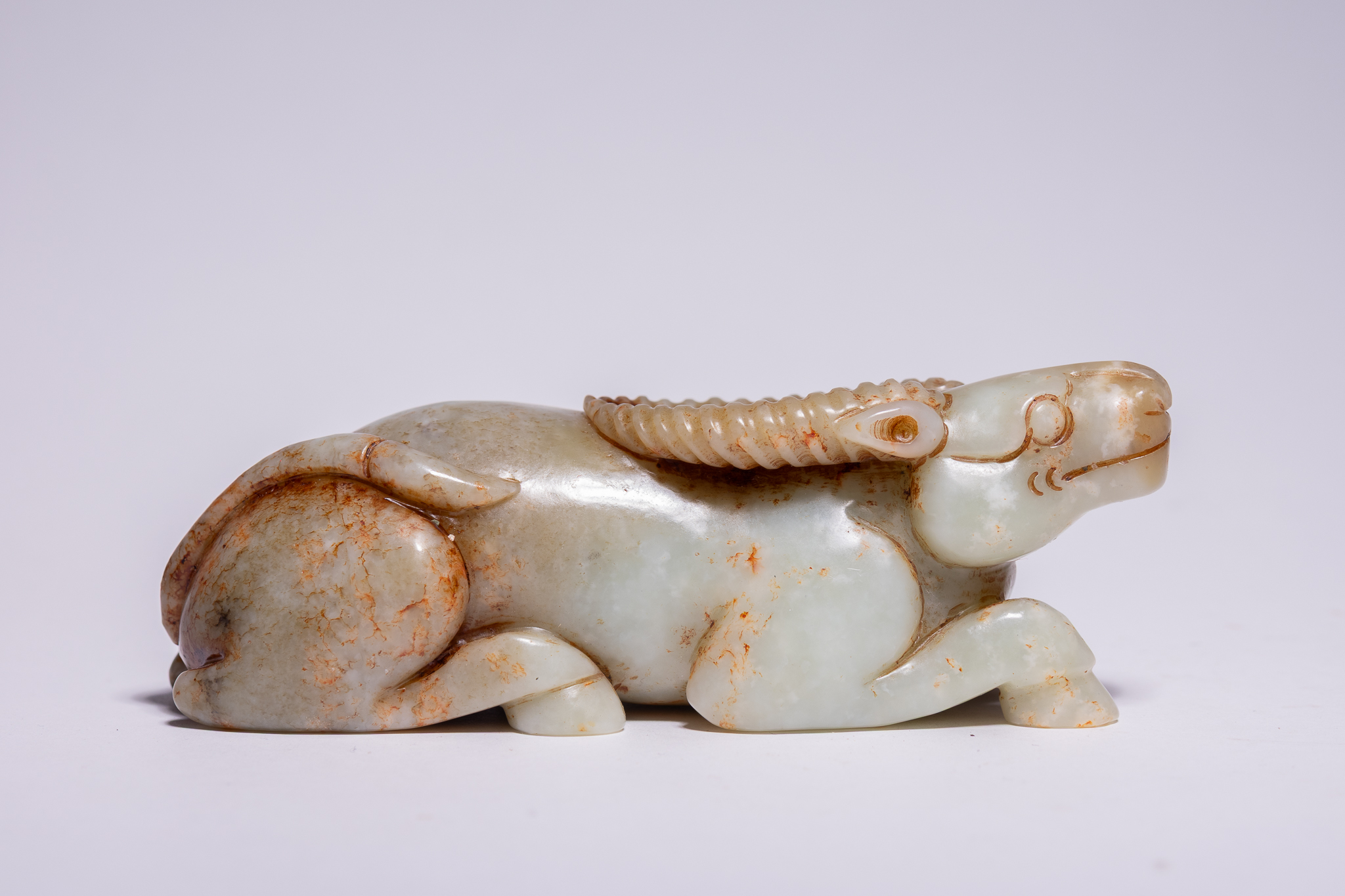 A CHINESE CELADON AND RUSSET JADE CARVING OF A RECUMBENT WATER BUFFALO.