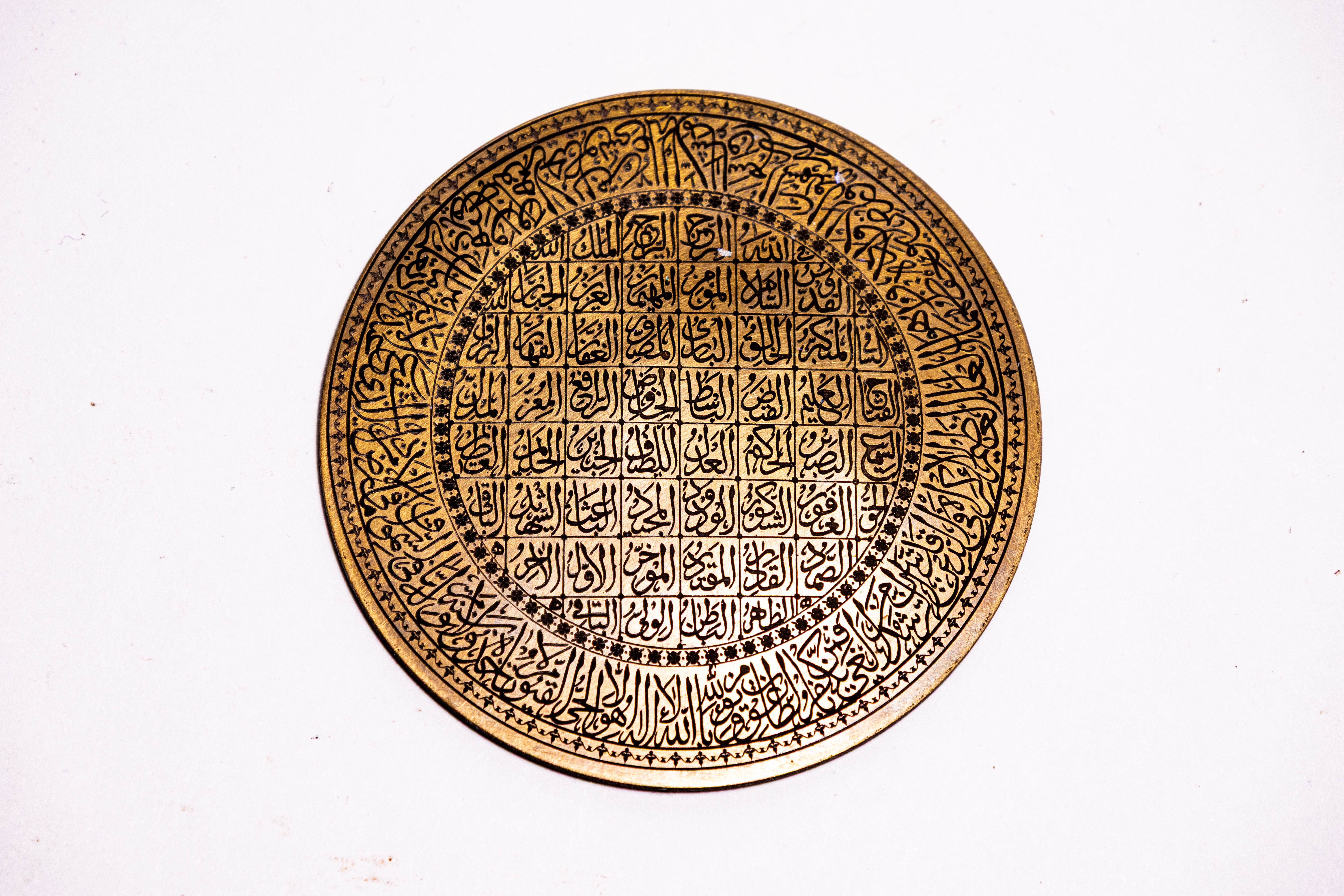 AN ENGRAVED BRASS ISLAMIC CALLIGRAPHIC PLAQUE FEATURING THE 99 NAMES OF ALLAH.