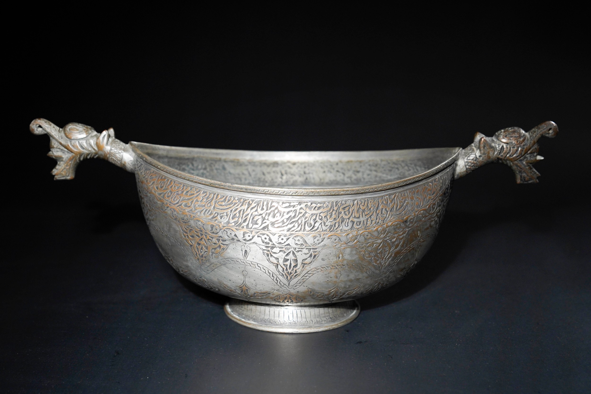 A QAJAR COPPER KASHKUL BEGGAR'S BOWL WITH DRAGON-HEAD TERMINALS, 19TH CENTURY.