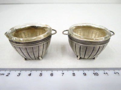 Pair of silver plated saltcellars, in the shape of small baskets, inside glass