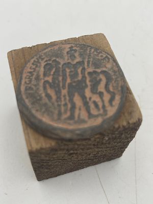 מטבע ברונזה רומי עתיק, ככל הנראה מסוג נומנוס (Nummus) או פוליס (Follis), המתאר דמויות שלטוניות.