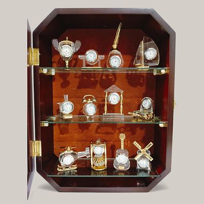 CRYSTAL. 12 CRYSTAL AND GILT METAL CLOCK MINIATURES IN DISPLAY CASE - wooden display case with 