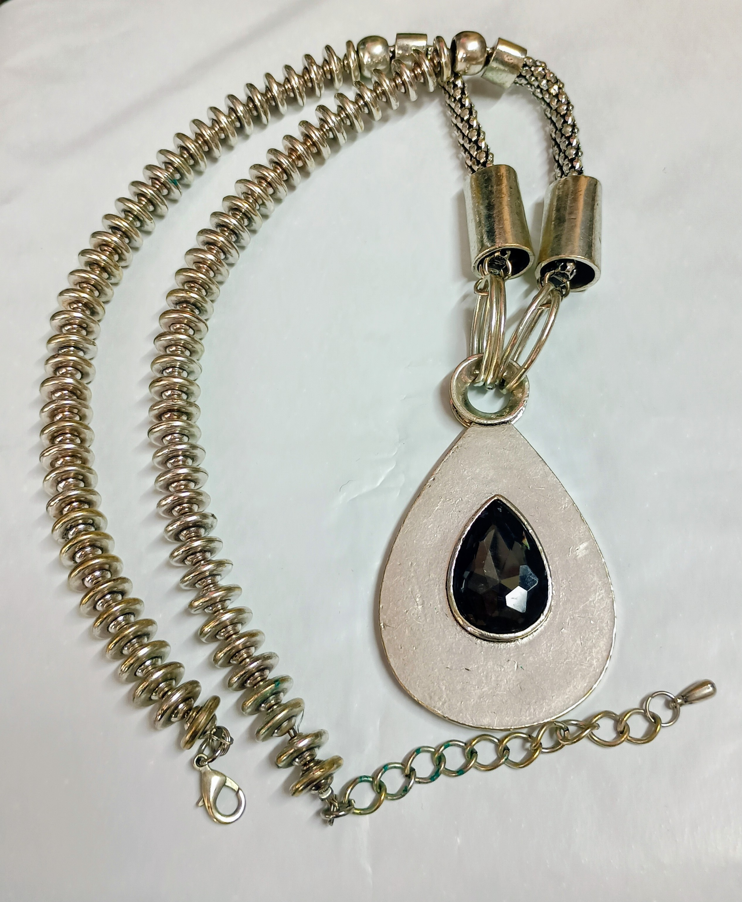 Large silver-tone pendant necklace on chunky chain and a teardrop-shaped charm with a dark stone