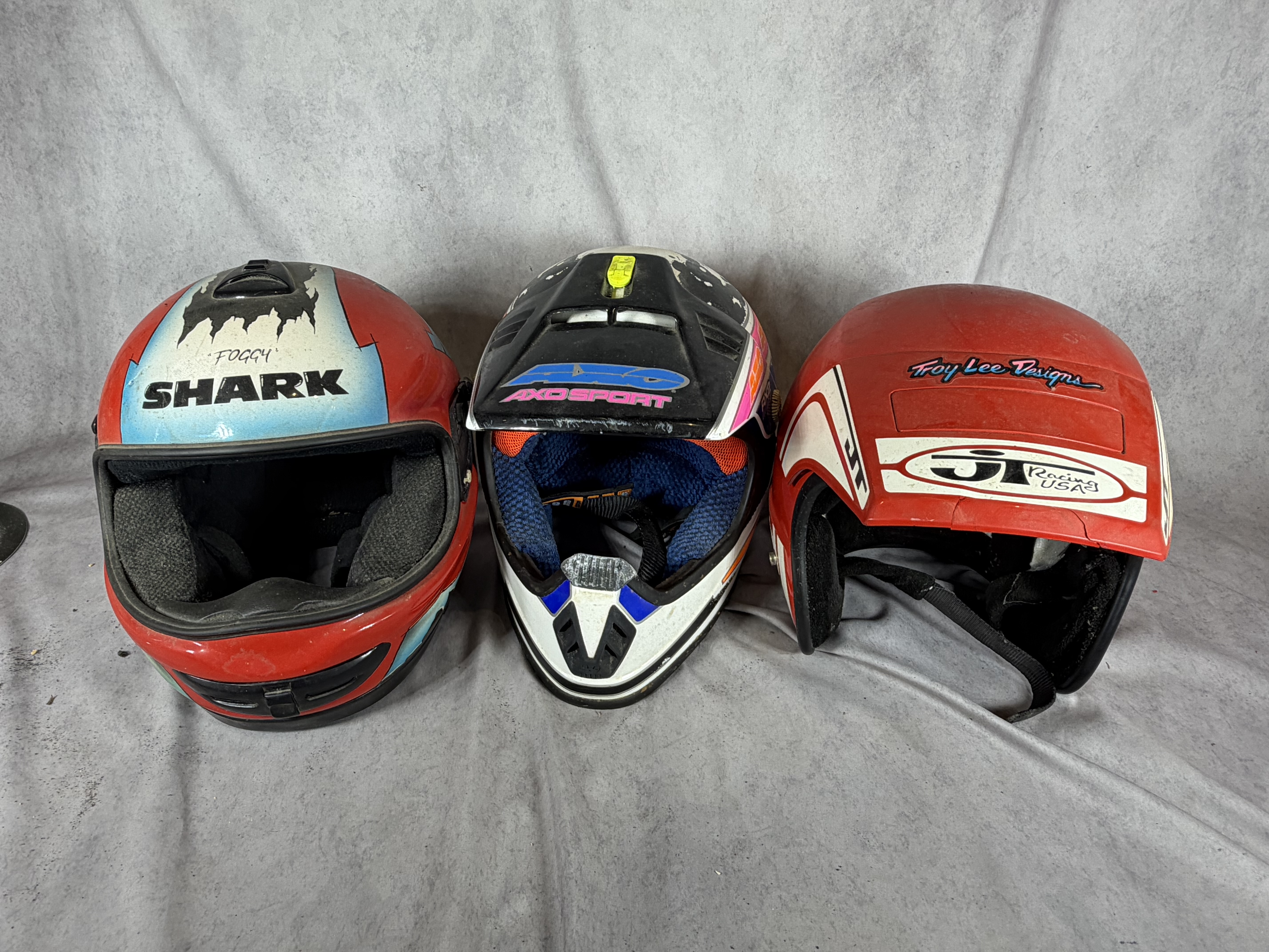 A Trio of Vintage Motorcycle Helmets Including Shark Carl Fogarty Replica, AXO Sport RX2, and Bell JT Racing USA