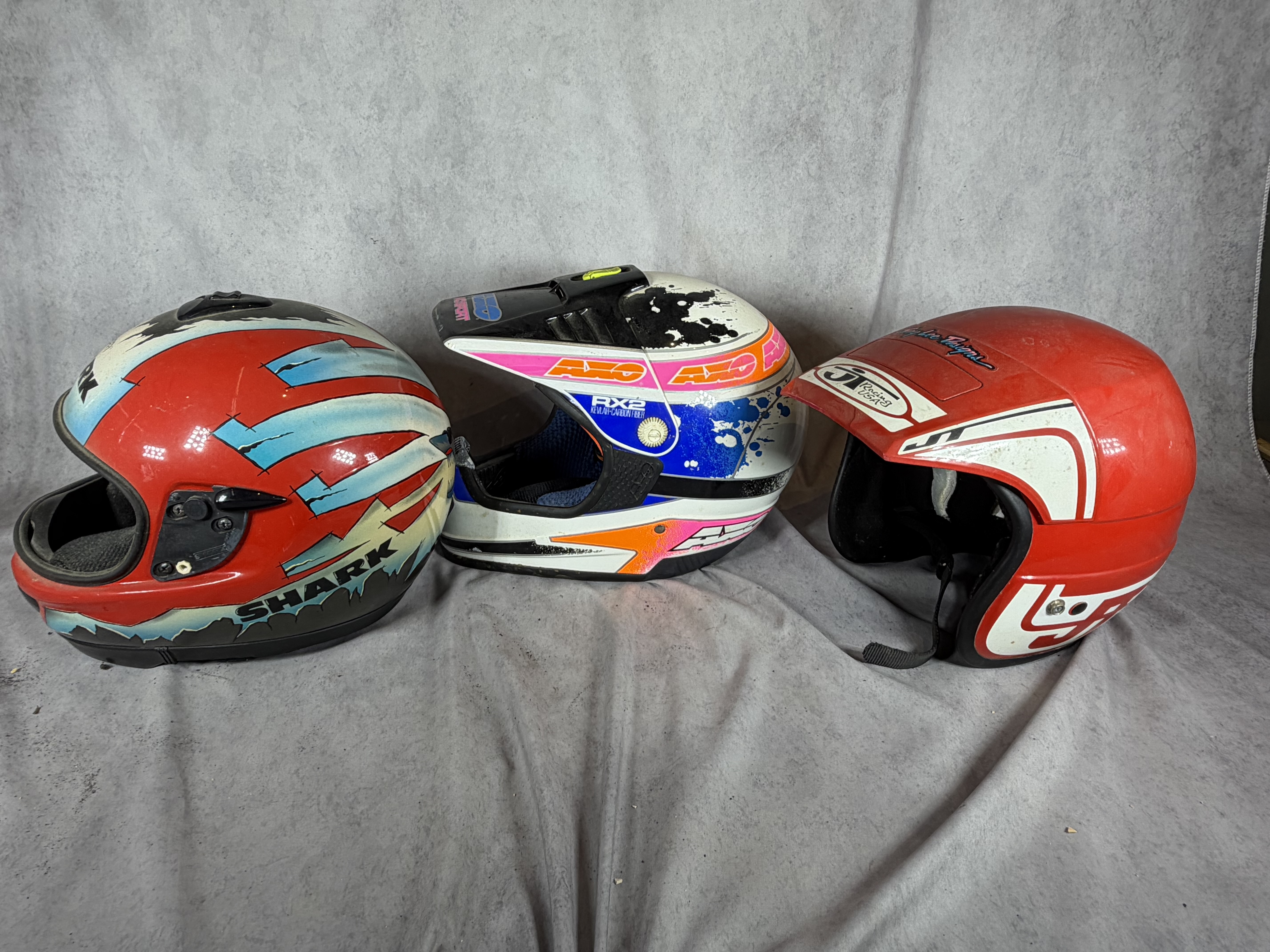 A Trio of Vintage Motorcycle Helmets Including Shark Carl Fogarty Replica, AXO Sport RX2, and Bell JT Racing USA