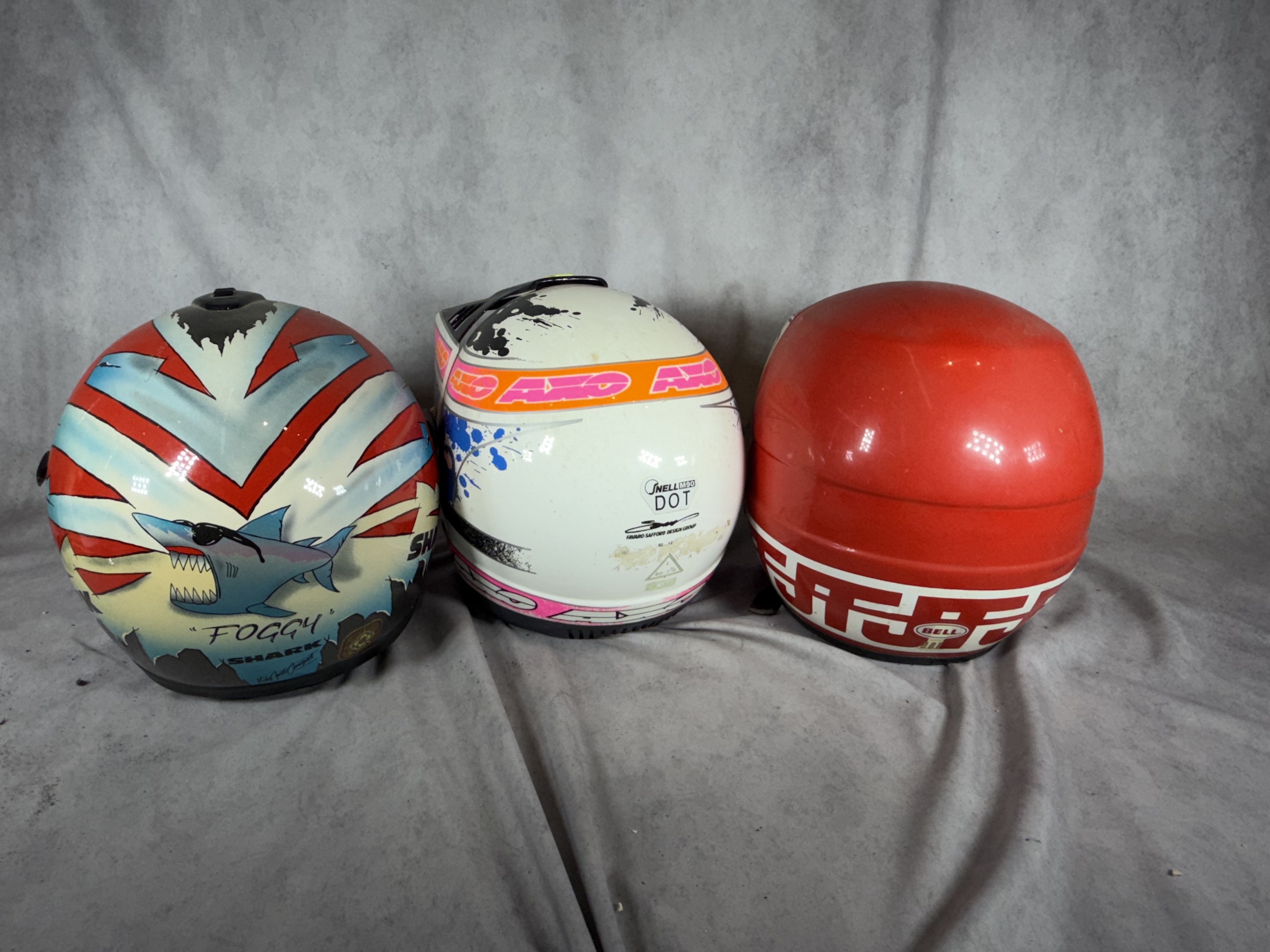 A Trio of Vintage Motorcycle Helmets Including Shark Carl Fogarty Replica, AXO Sport RX2, and Bell JT Racing USA