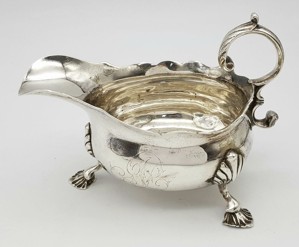 An Antique Georgian Sterling Silver Sauce Boat. C scroll handle and standing on three webbed 